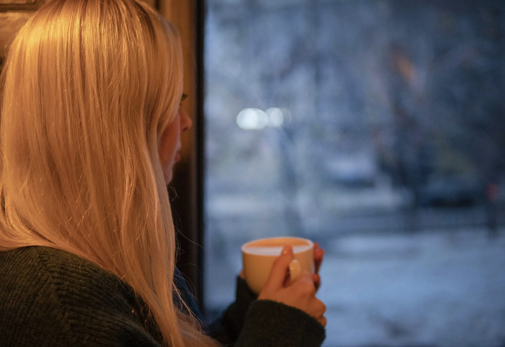 woman holding a mug while staring out the window